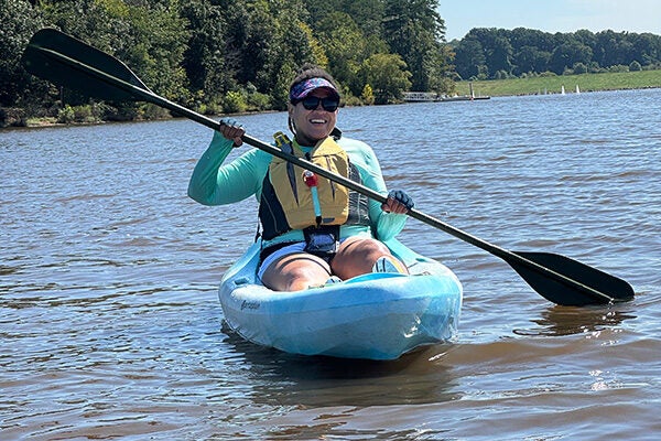A woman in a life vest is paddling at Lake Crabtree in a blue kayak.