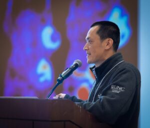 Zibo Li standing at podium speaking at conference.