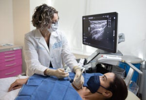 Genevieve Woodard performed an ultrasound on a patient. She and the patient, who is lying on a hospital bed, are both looking at the screen.